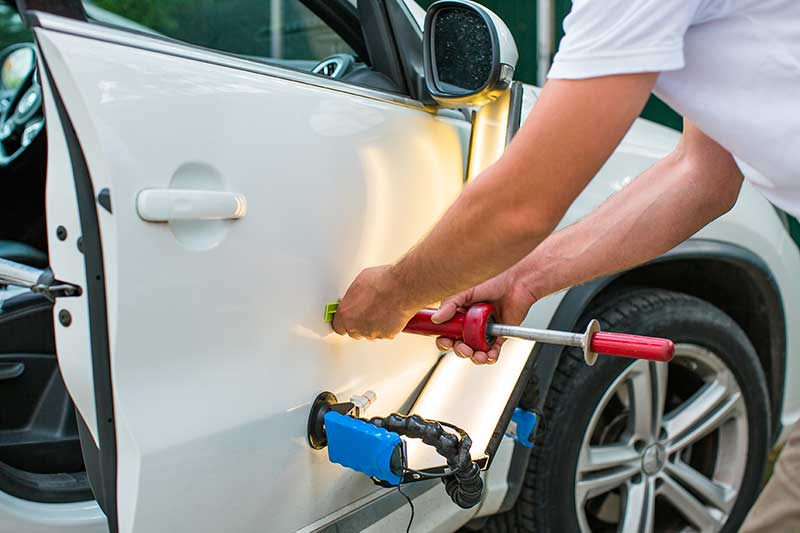 Technician performing dent repair on a vehicle door.